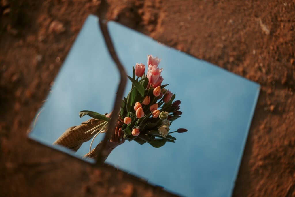 Mirror reflects flowers against a blue sky.