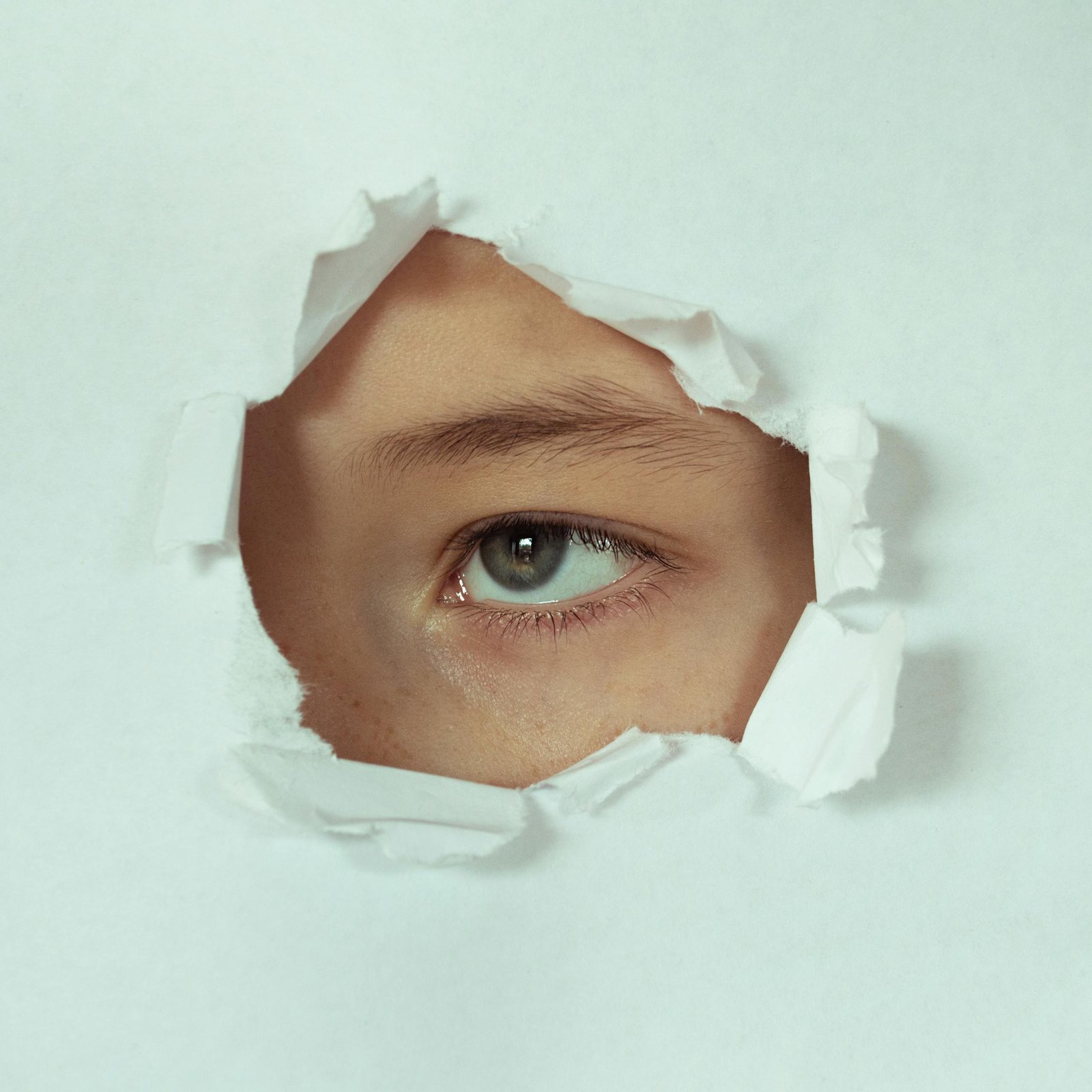 A close-up of an eye peeking through a hole in white paper, conveying curiosity and mystery.