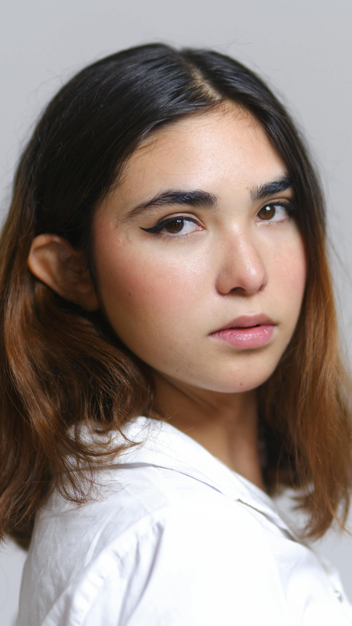 Close-up portrait of a young woman with subtle makeup and neutral background.
