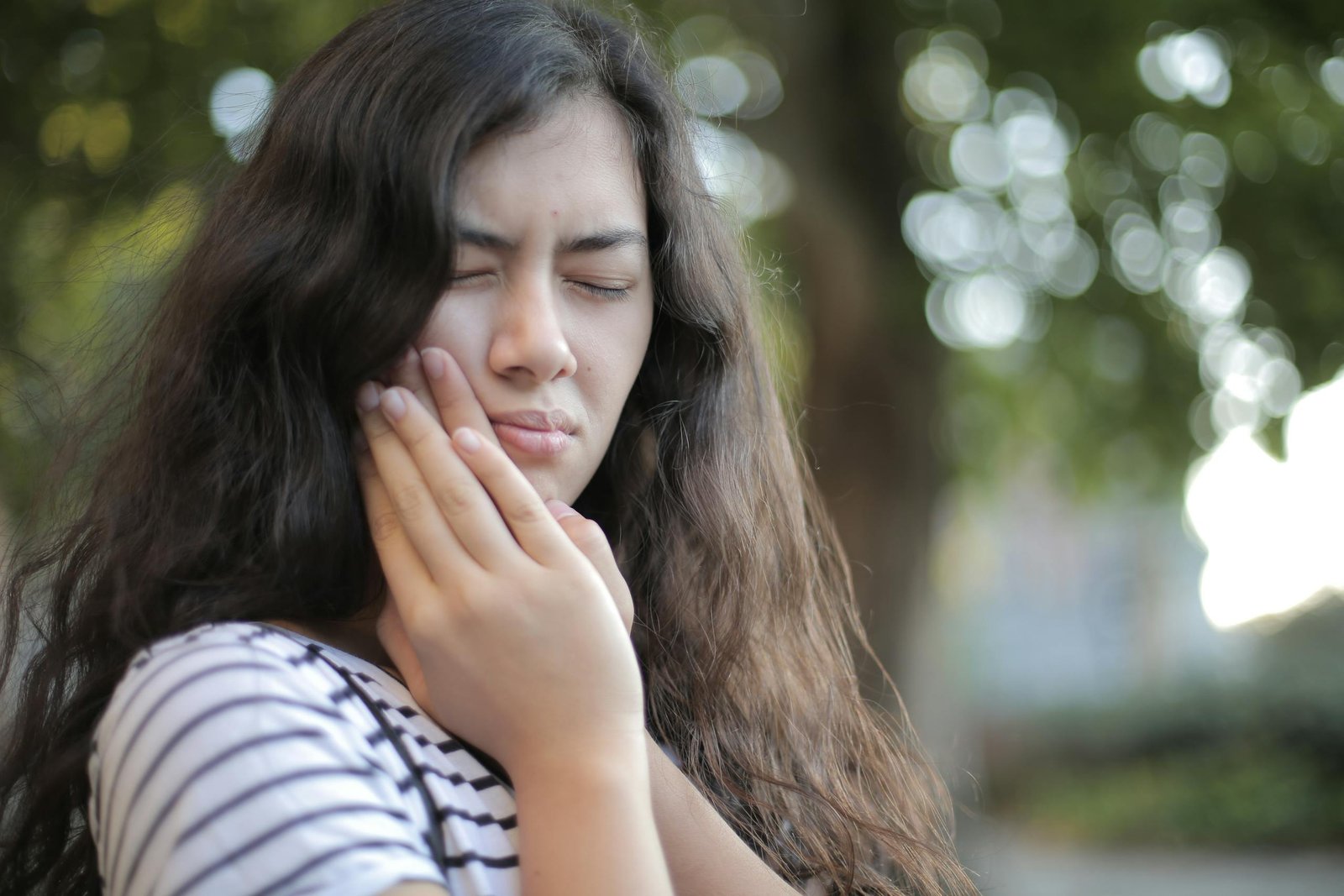 Portrait of a young woman feeling toothache, showing discomfort outdoors with a pained facial expression.