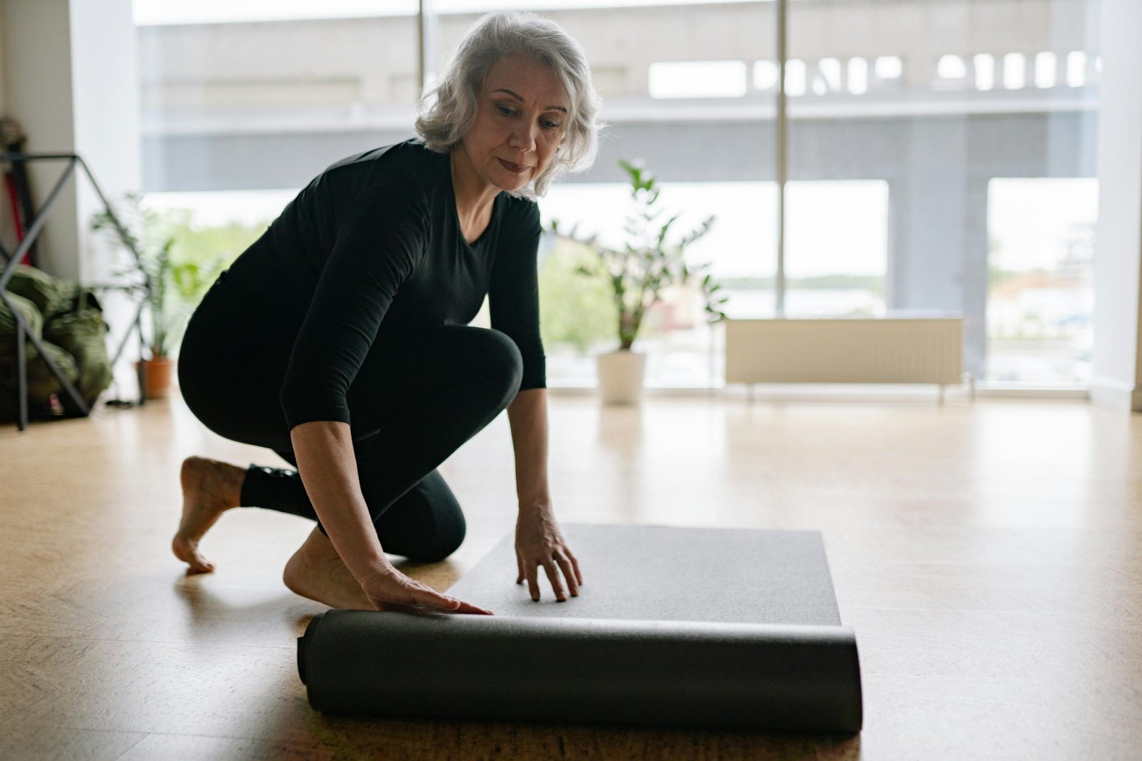 Senior woman setting up yoga mat in bright studio, preparing for exercise.