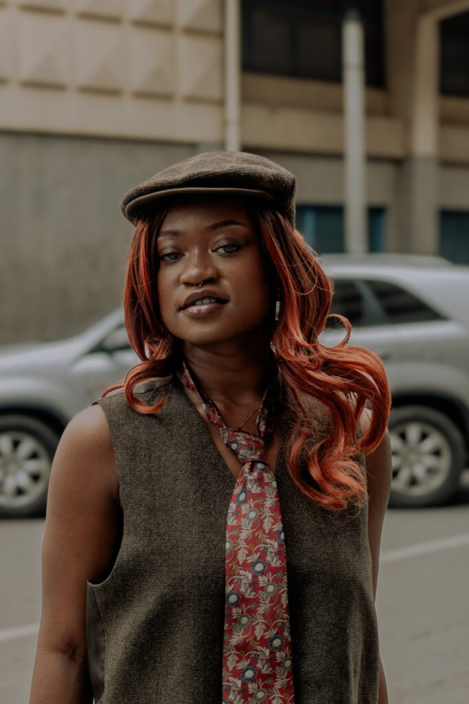 A woman with red hair wearing a tie and a hat