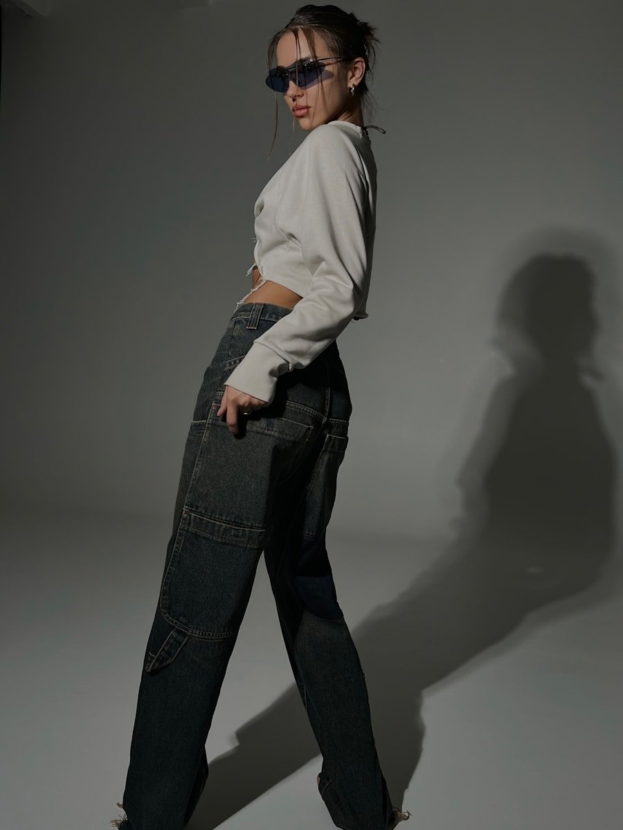 A woman poses in stylish clothing and sunglasses.