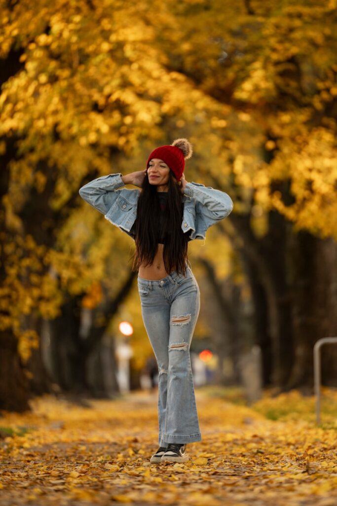 A woman in jeans and a red hat walking down a leaf covered road