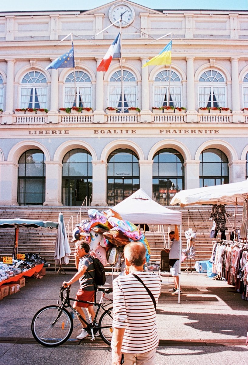 A market with flags is in front of a grand building.