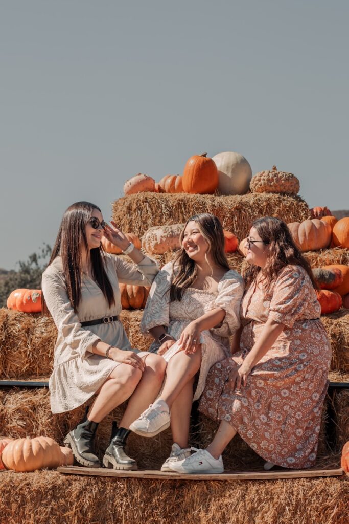 three women sitting on hay bales with pumpkins in the background