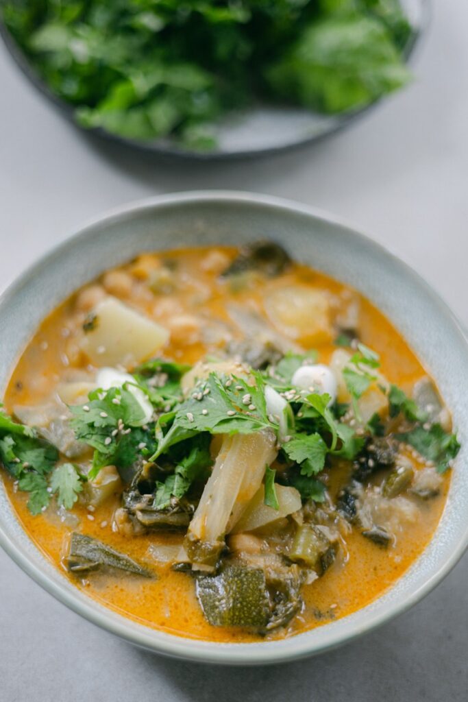 a white bowl filled with soup next to a plate of greens