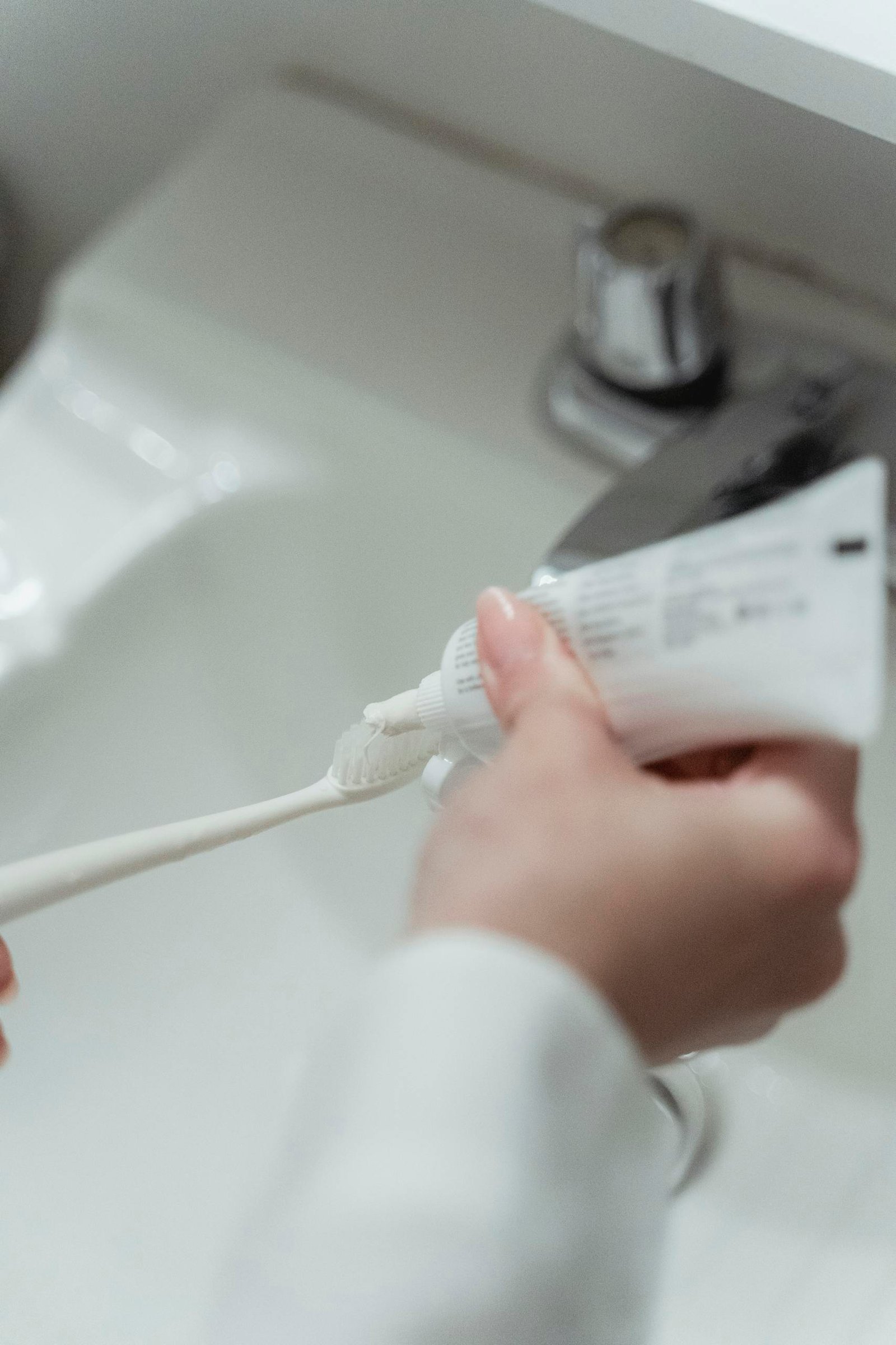 A close-up of a hand squeezing toothpaste onto a toothbrush at the sink.