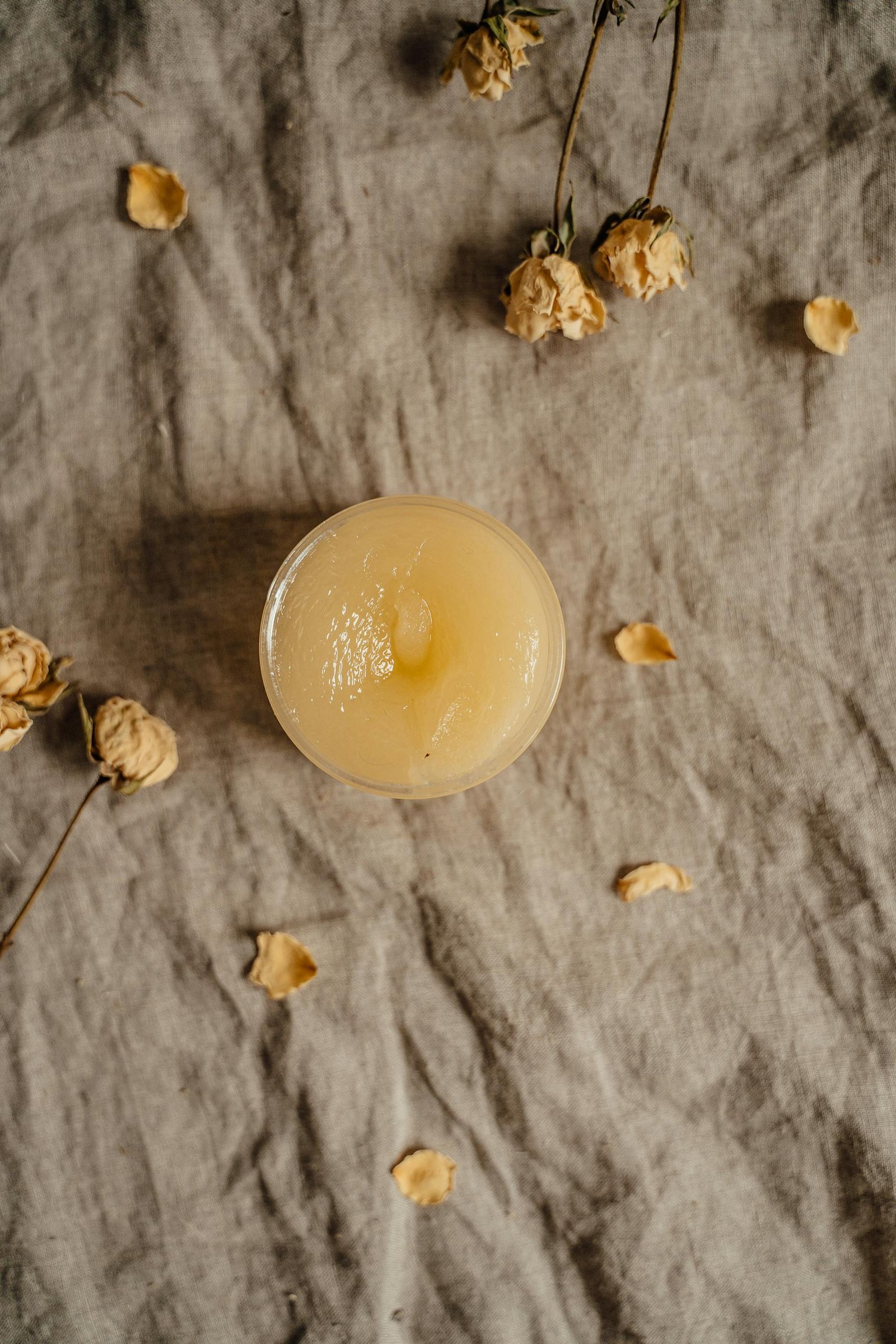A top-view image of a natural ointment surrounded by dried roses, ideal for skincare concepts.