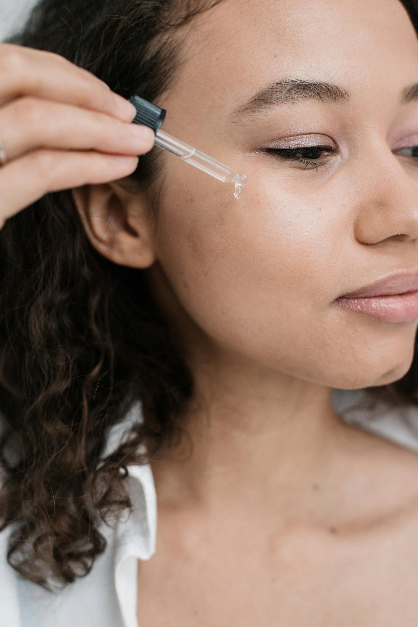 A young woman applying skincare serum to her face with a dropper for a beauty treatment.