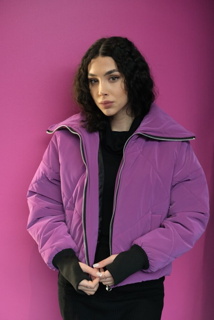 a woman in a purple jacket standing against a pink wall