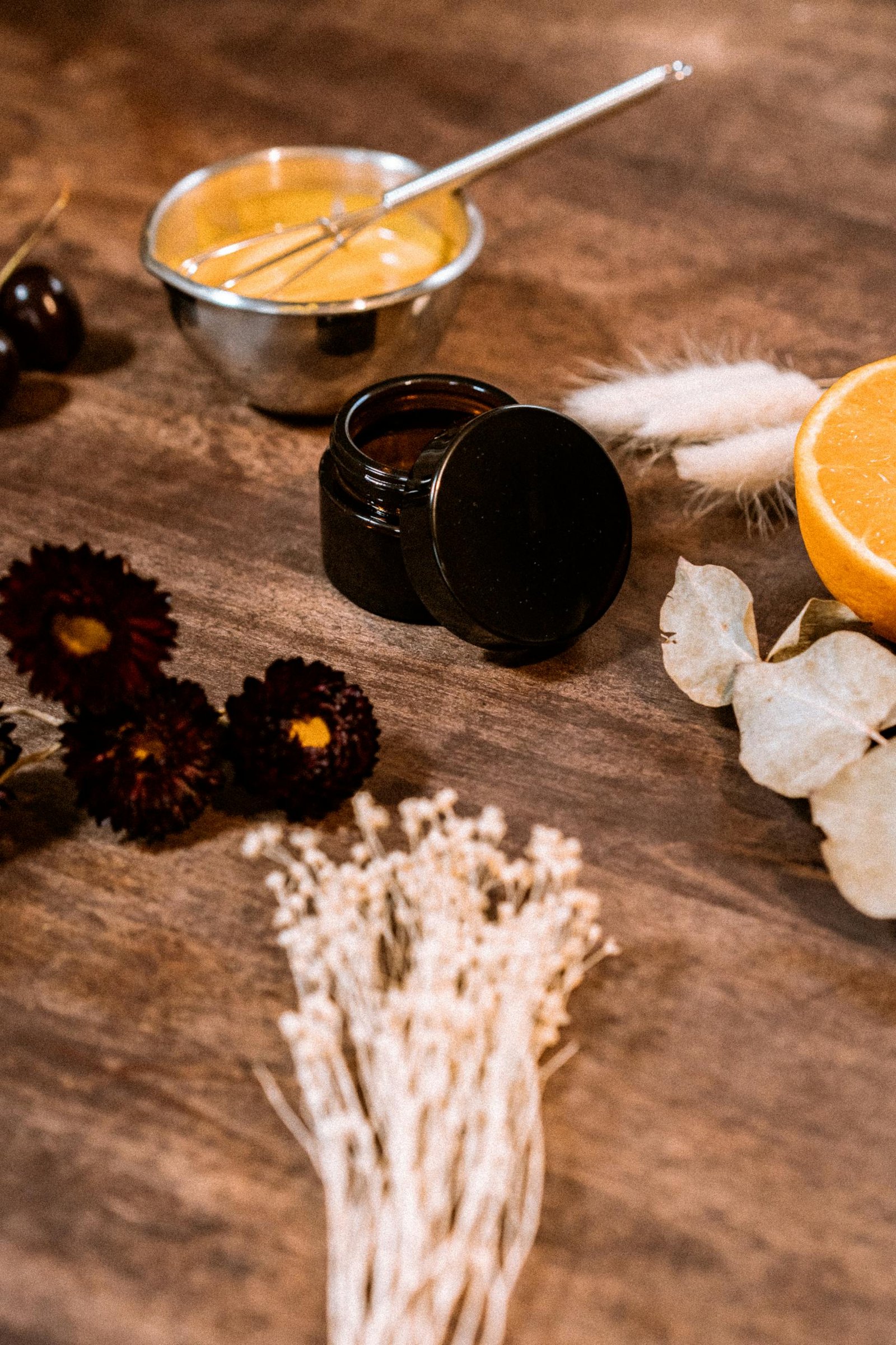 Top-down view of natural cosmetic ingredients surrounded by dried flowers and an orange slice.