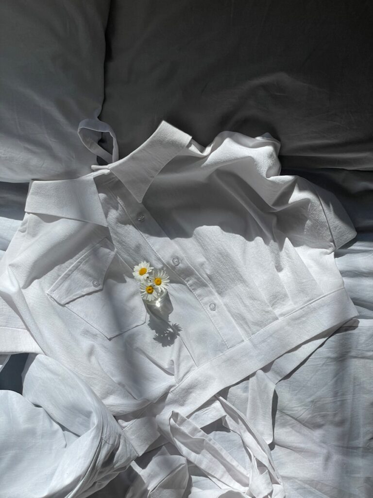 a white shirt laying on top of a bed next to a flower