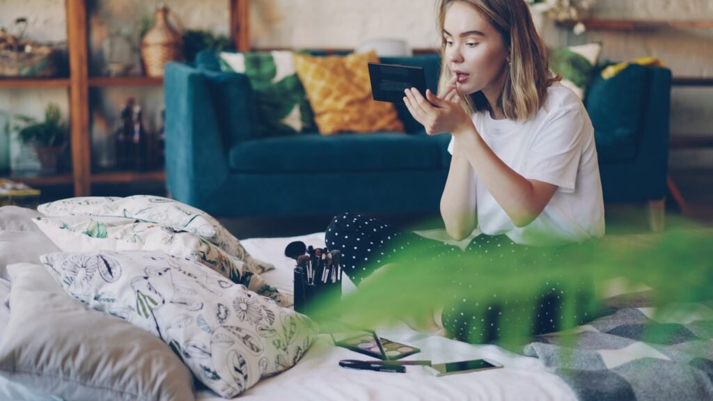 Young woman applying lipstick in bedroom