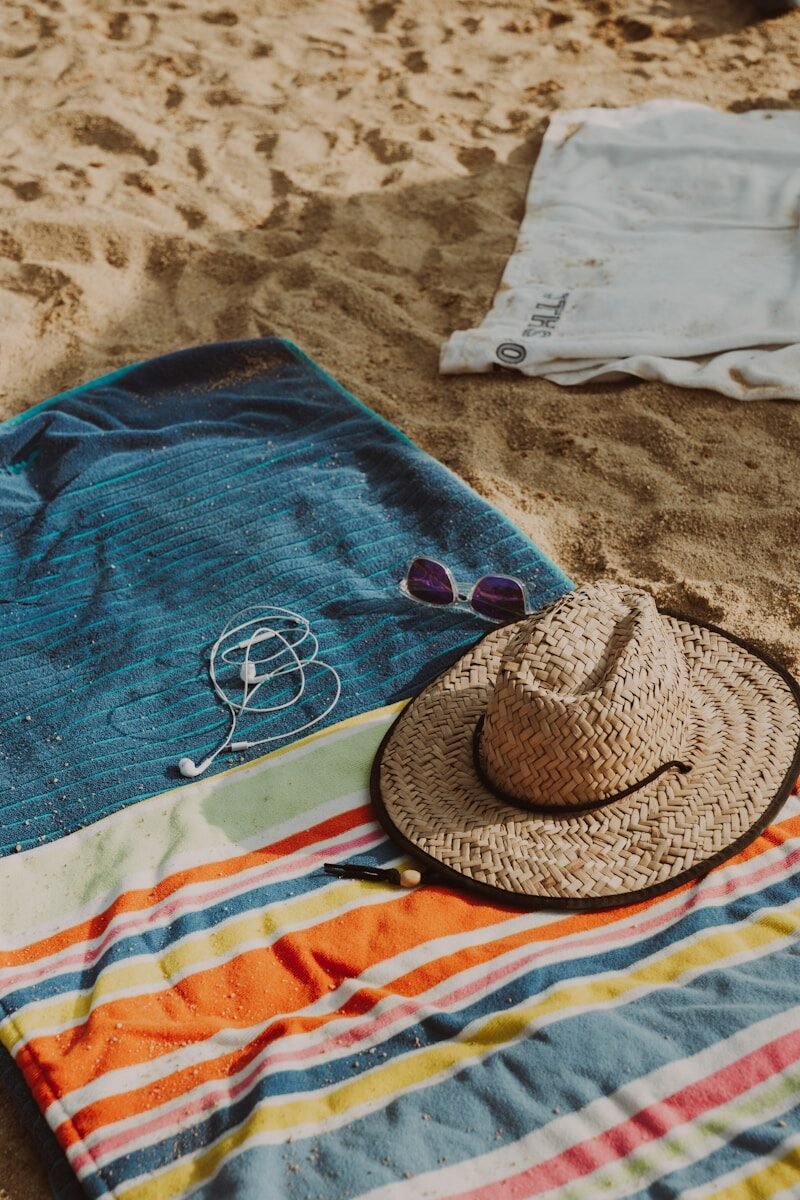 A beach towel, hat, and sunglasses on the sand